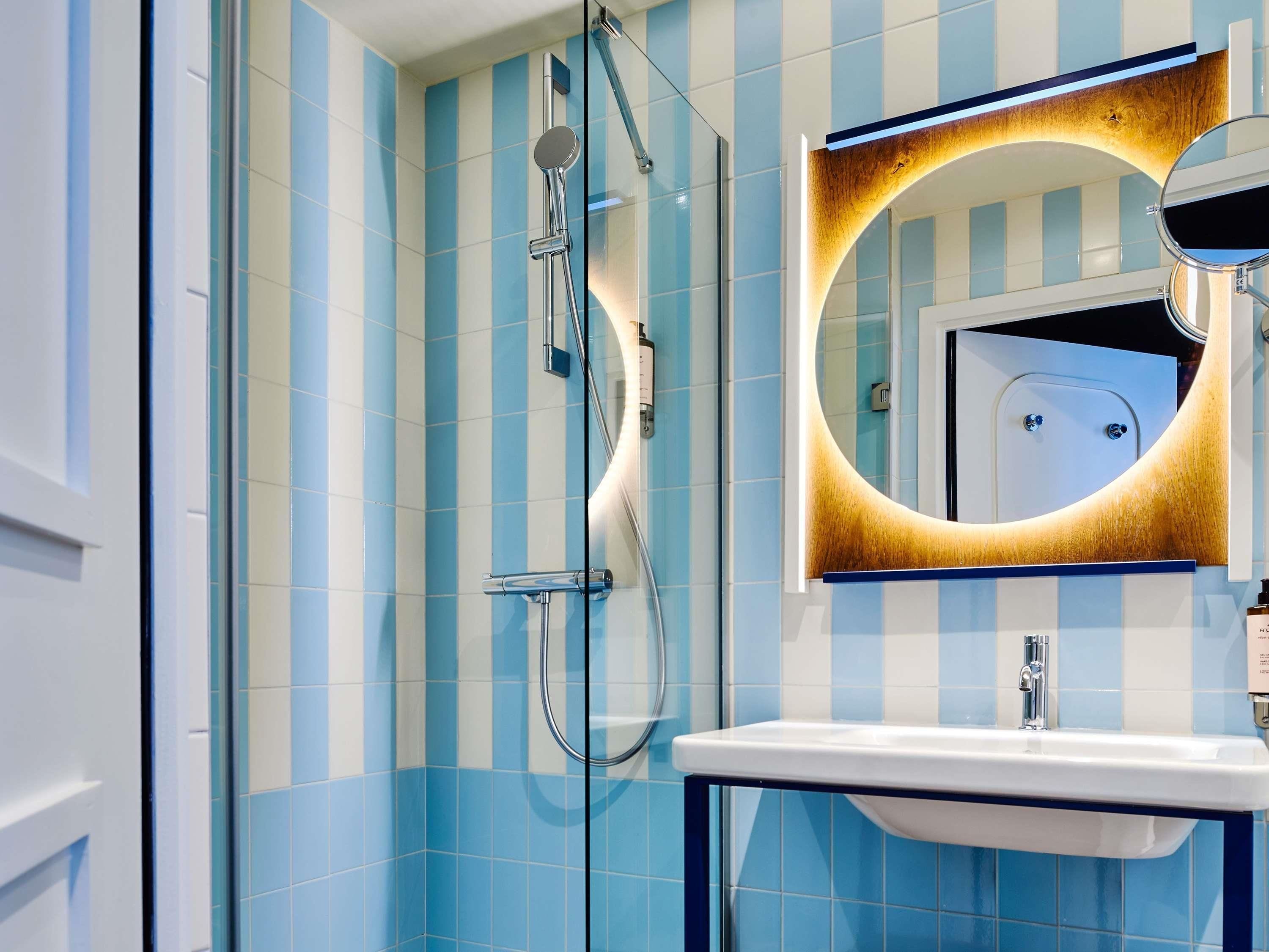 A bathroom with blue and white striped tiles, a glass shower enclosure, a white sink, and a mirror with a wooden frame.