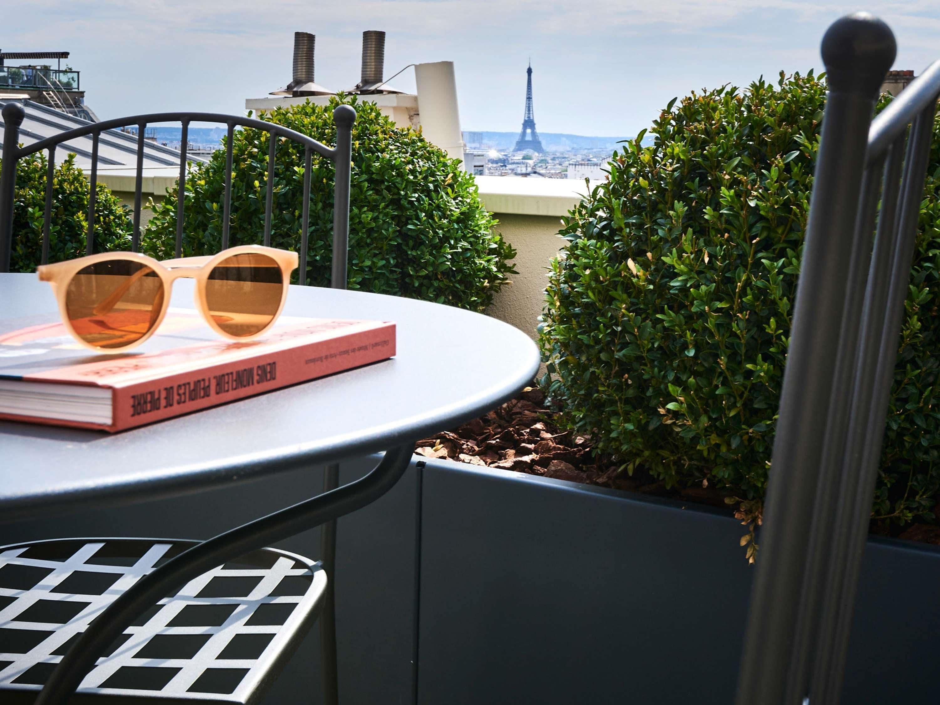 A table with a book and sunglasses, a metal chair, and a view of the Eiffel Tower.