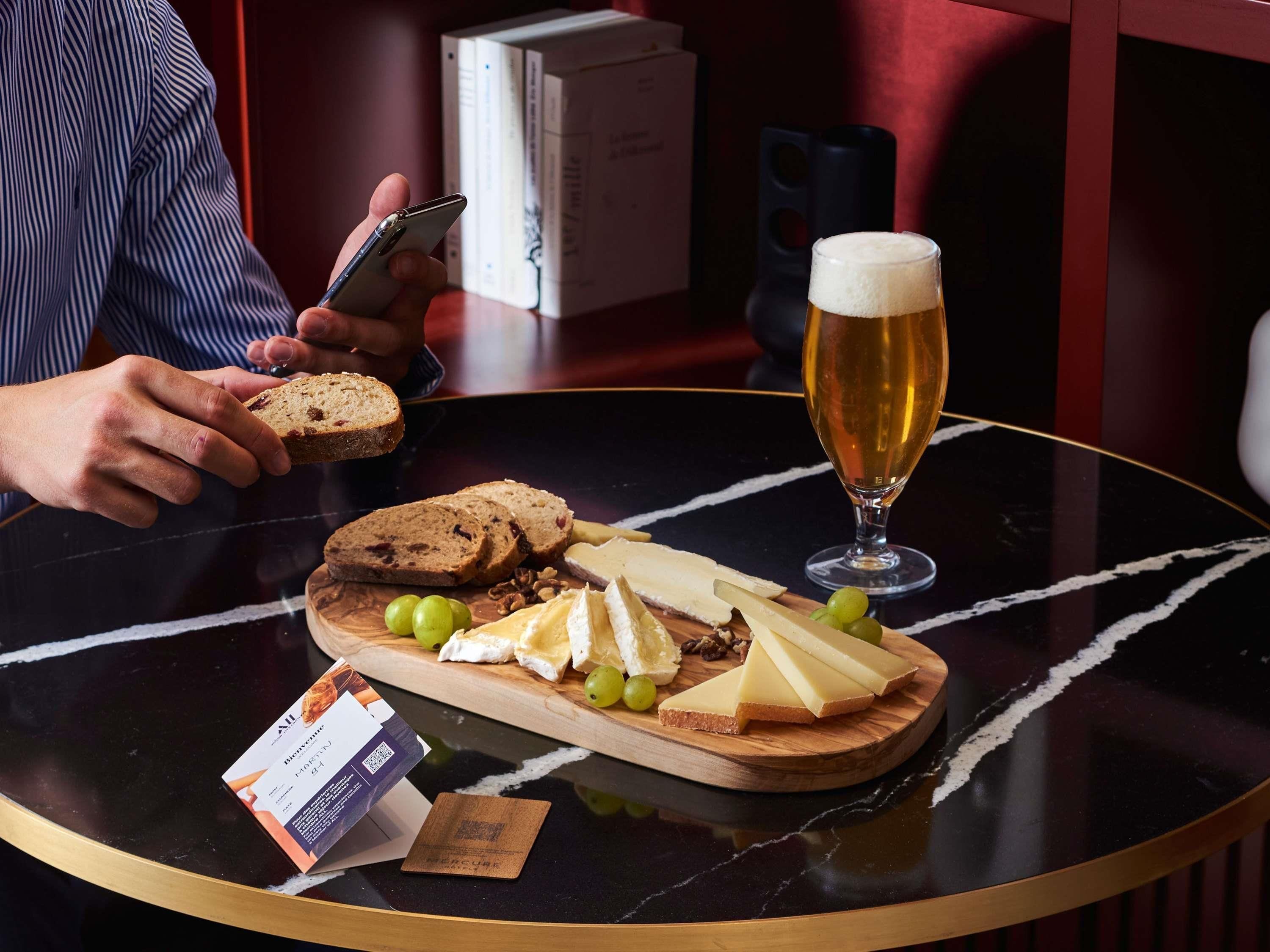 A round table with a cheese board, a glass of beer, and a person using a smartphone.