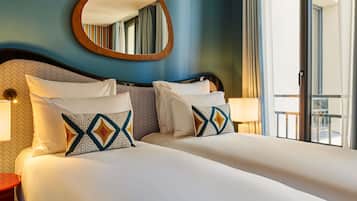 Habitación de hotel con una cama grande, dos mesitas de noche, un espejo redondo y vistas al exterior.
