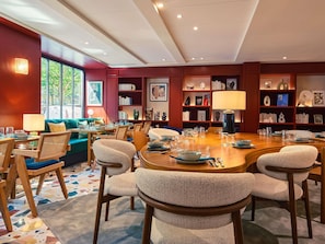 A dining area with a round wooden table, multiple chairs, and a bookshelf filled with books and decorative items.