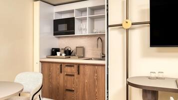 A compact kitchen with a microwave, kettle, and coffee maker, wooden cabinets, a sink, and a round table with glasses.