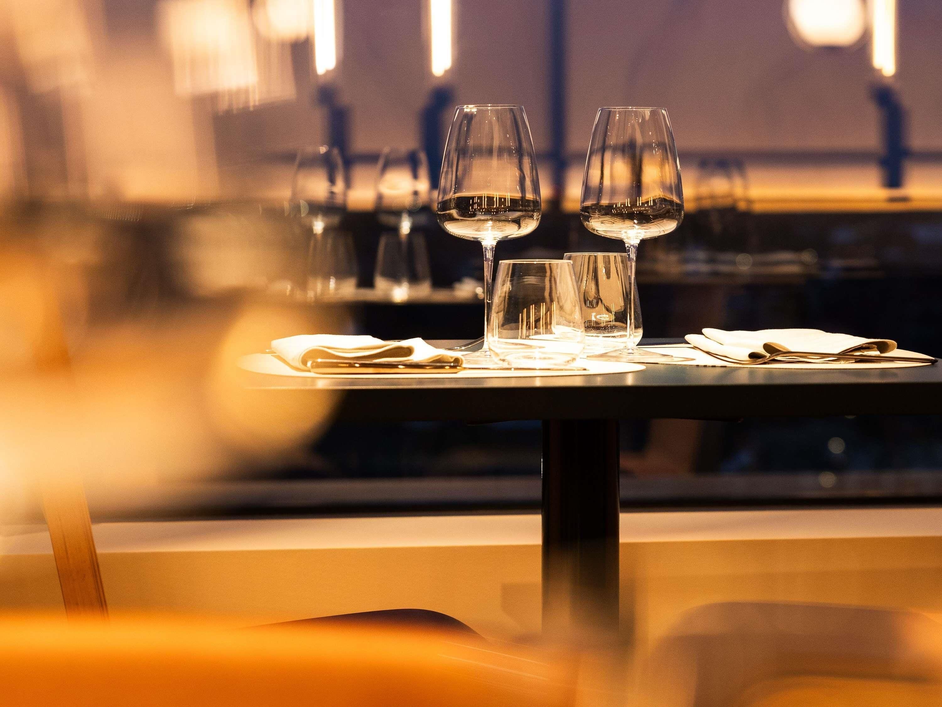 Et spisebord med tre vinglas og en serviet, placeret i en restaurant med dæmpet belysning og moderne indretning.