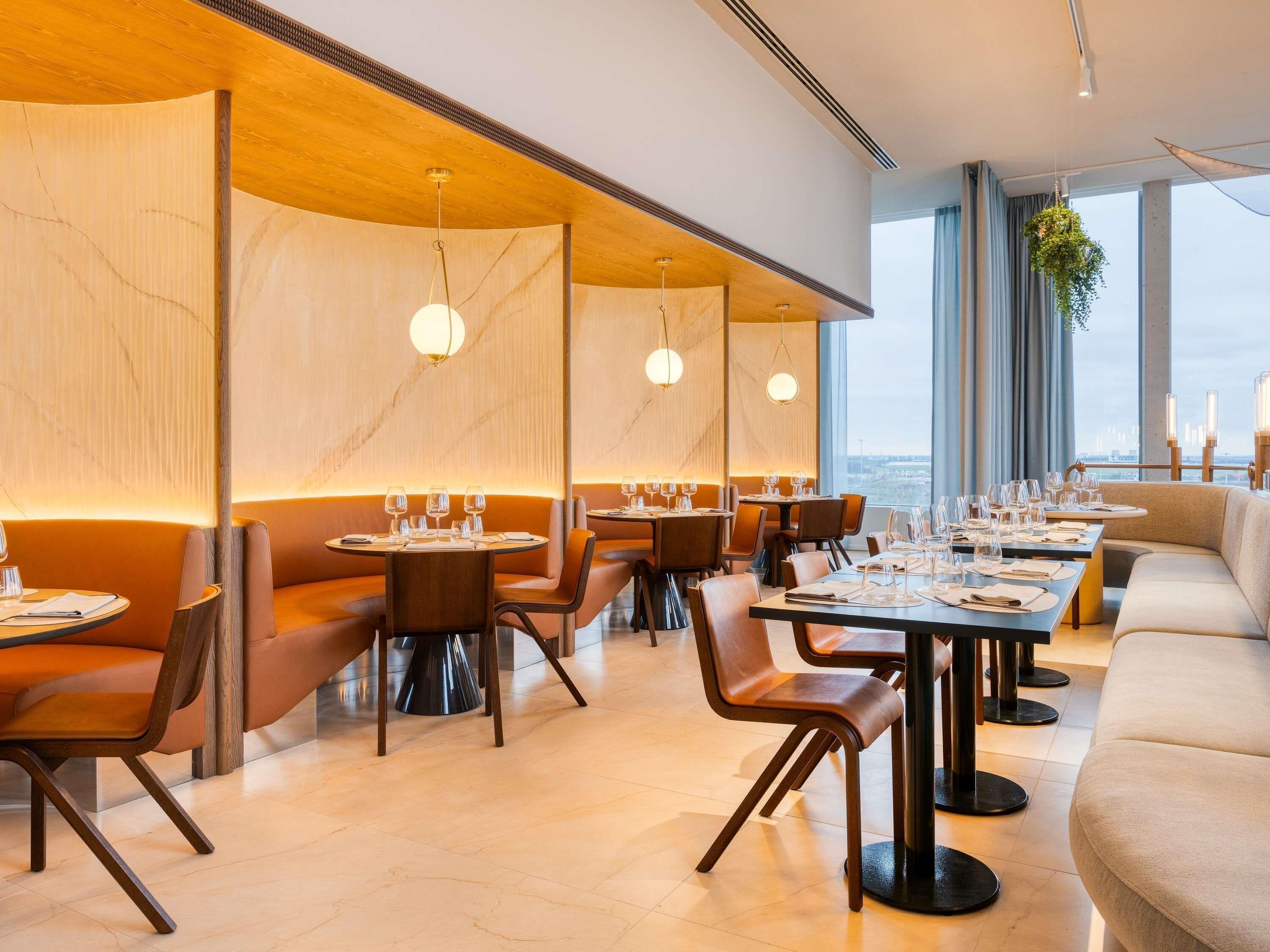 Un restaurant moderne avec des tables rondes, des sièges rembourrés et des luminaires suspendus.