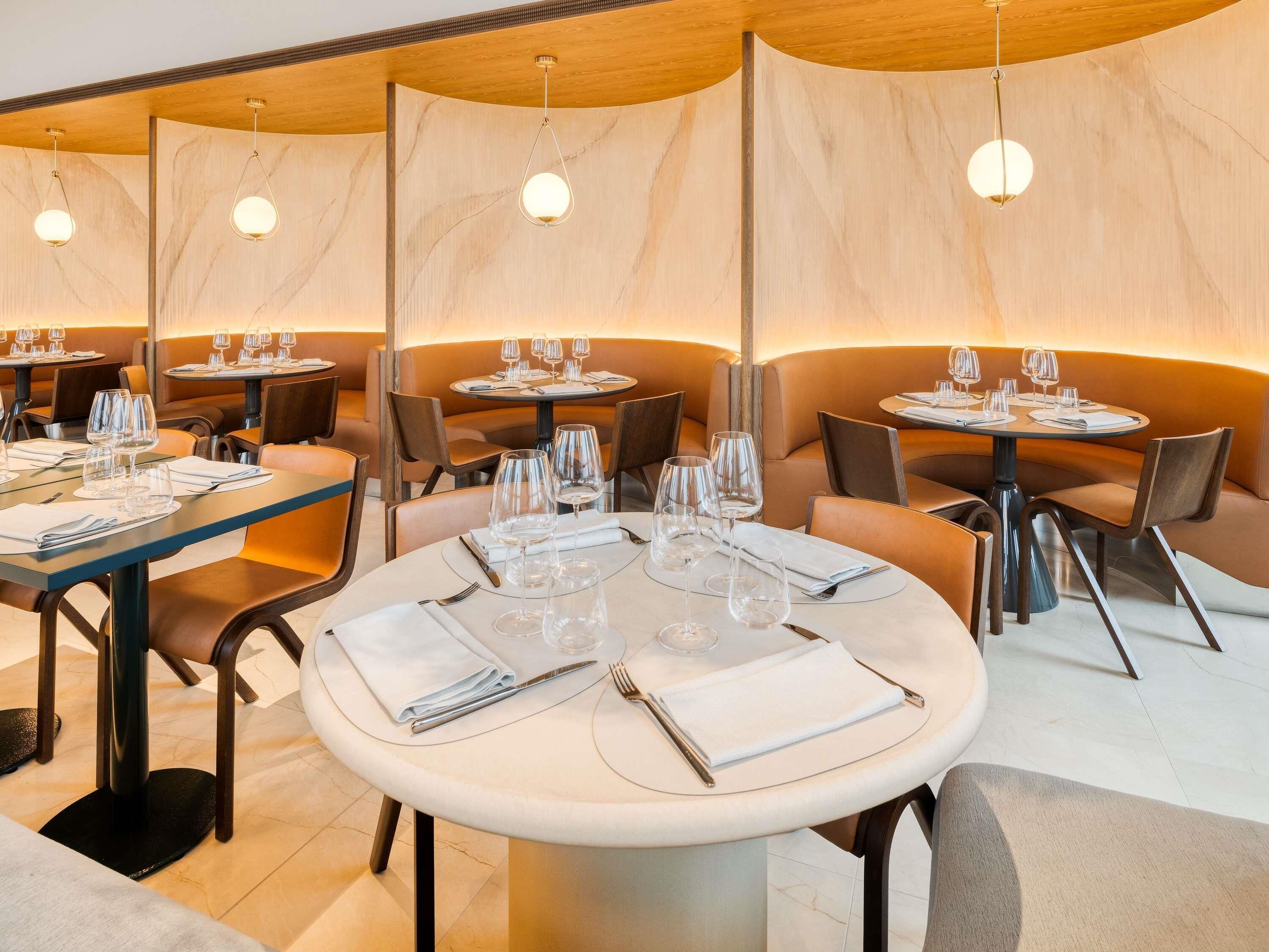 A restaurant with round tables, chairs, and hanging pendant lights.