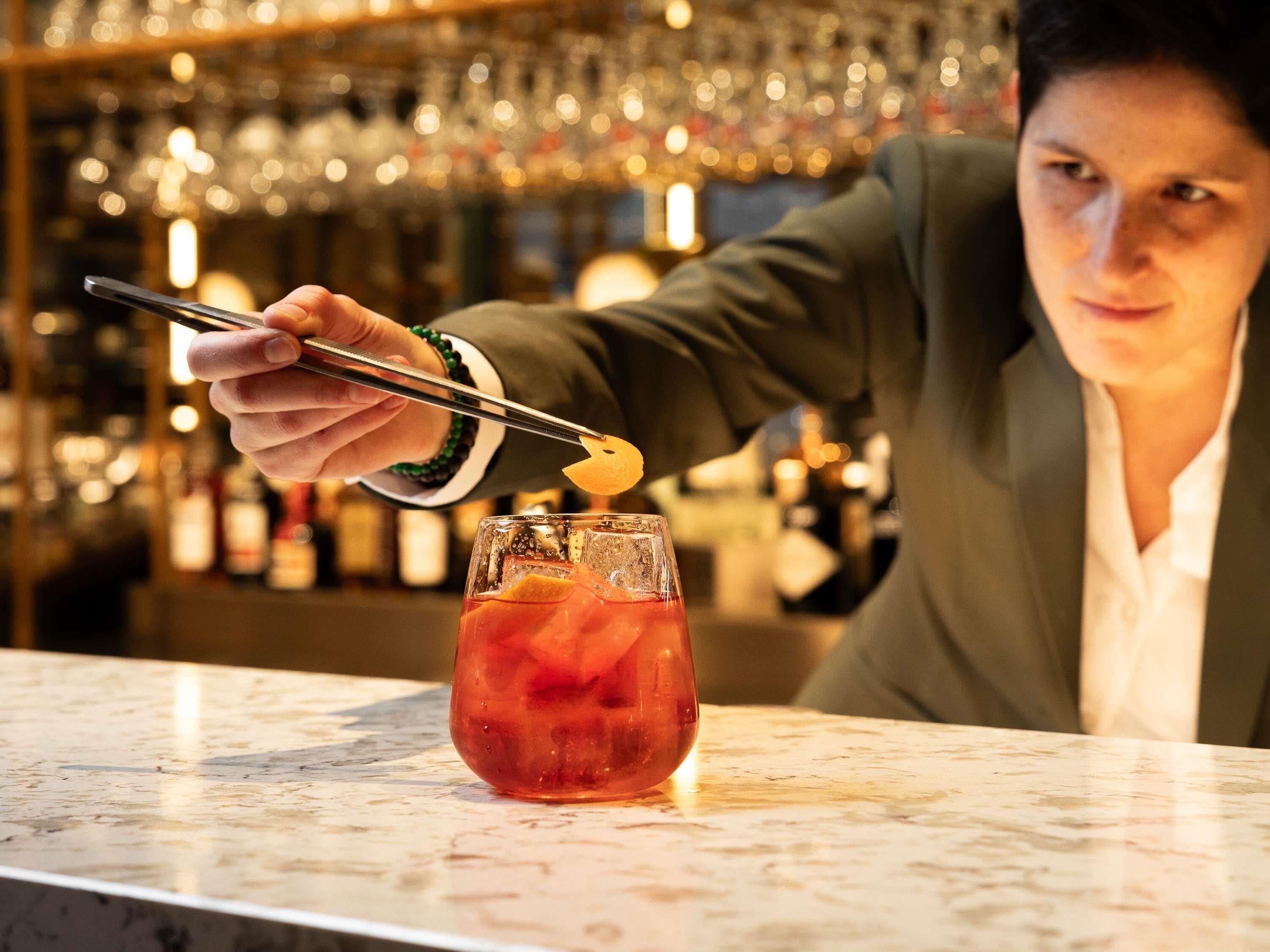 A person in a suit preparing a drink with a cocktail shaker and a spoon.