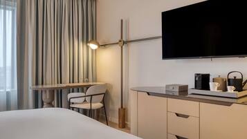 A hotel room with a bed, a desk with a chair, a television, and a minibar.