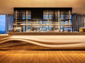 Eine Bar mit einer Marmor-Arbeitsplatte, mehreren Flaschenregalen, Gläsern und Blick auf die Stadt.