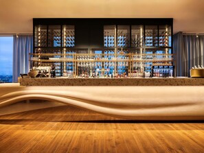 A bar area with a marble countertop, multiple shelves of bottles, glasses, and a view of the city. - Mövenpick hotel Brussels Airport  (Zaventem)