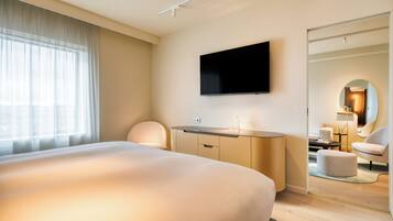 A hotel room with a large bed, a flat-screen TV mounted on the wall, a desk with a lamp, and a mirror.