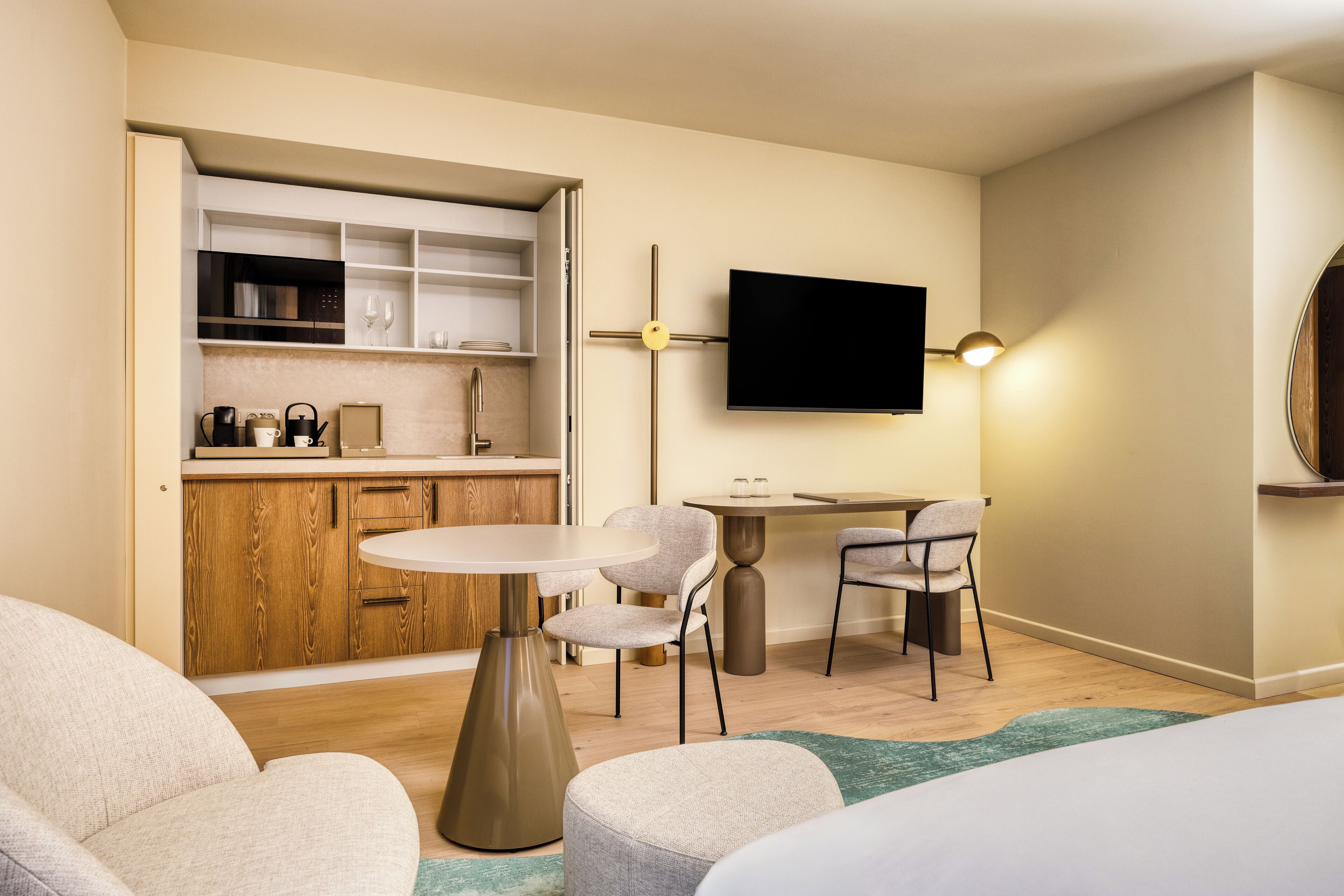 Una habitación de hotel moderna con kitchenette, un televisor de pantalla plana, una mesa de comedor redonda, dos sillas, un sofá y una cama.