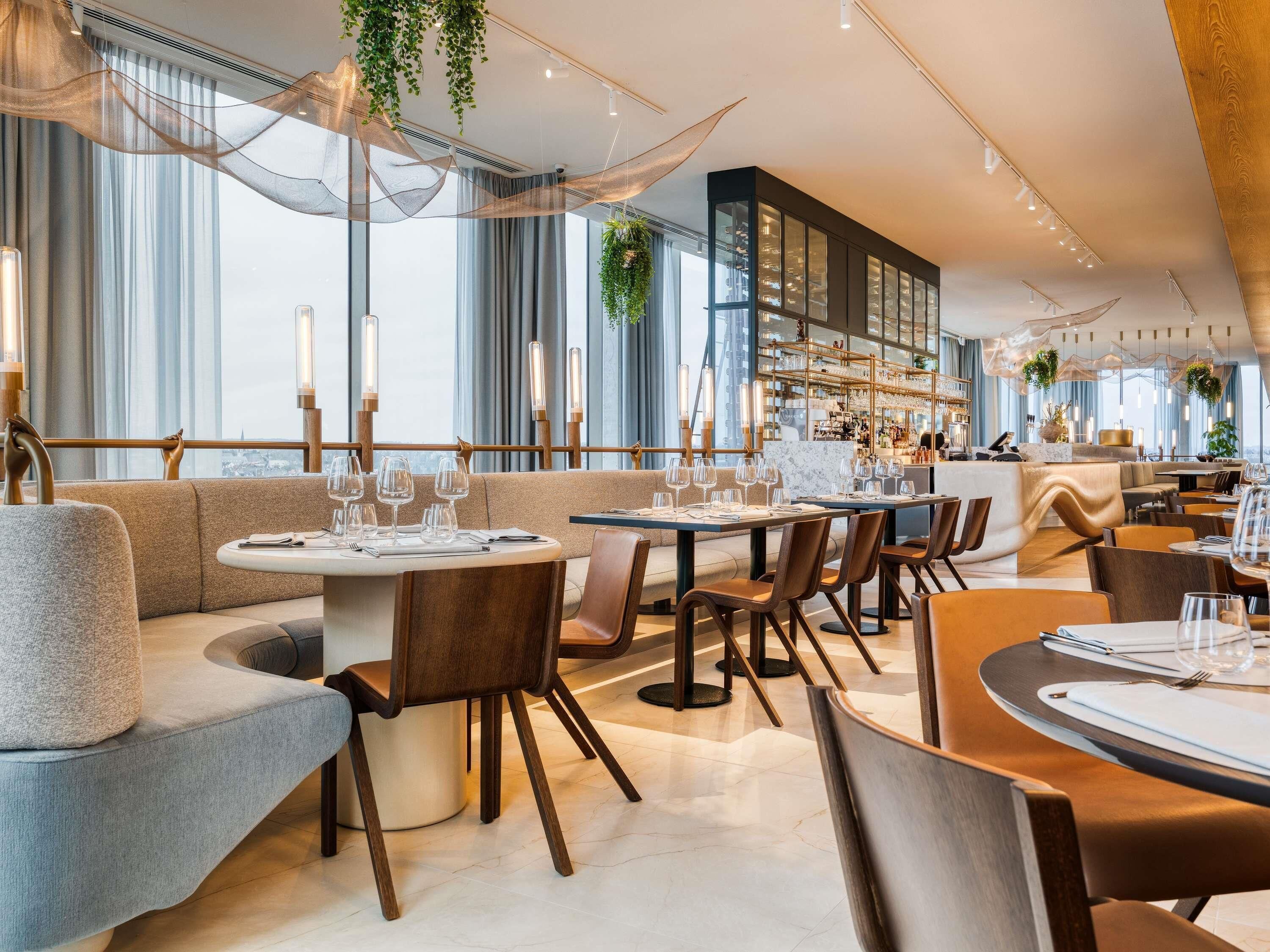 Un interior de restaurante moderno con mesas redondas, asientos acolchados y una zona de bar.