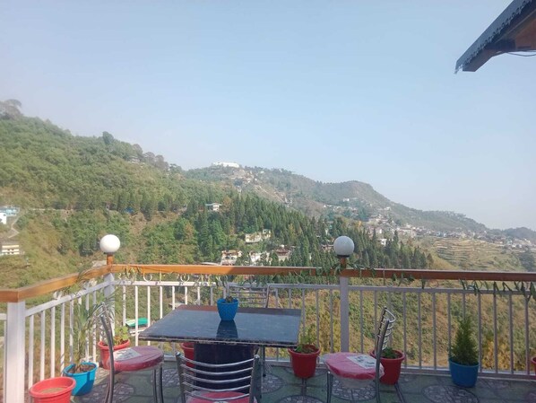 Un balcone con tavolo e sedie, piante in vaso e vista su un paesaggio collinare con edifici.