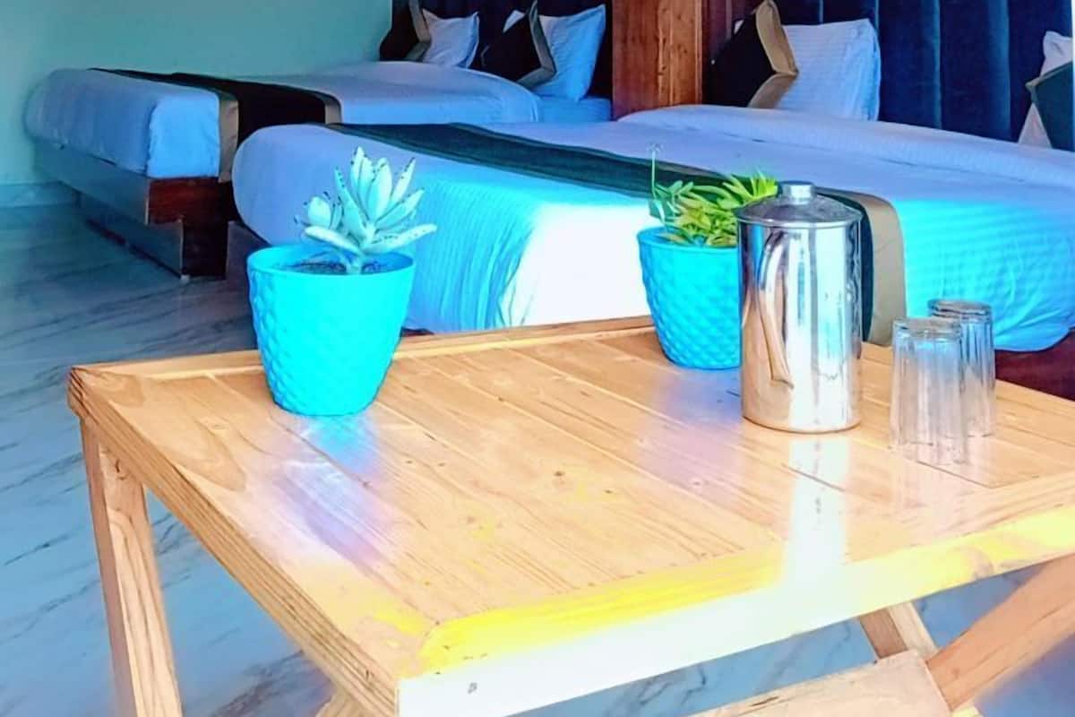 A hotel room with two beds, wooden ceiling, ceiling fans, wall-mounted lights, and a small table with a pitcher and glasses.