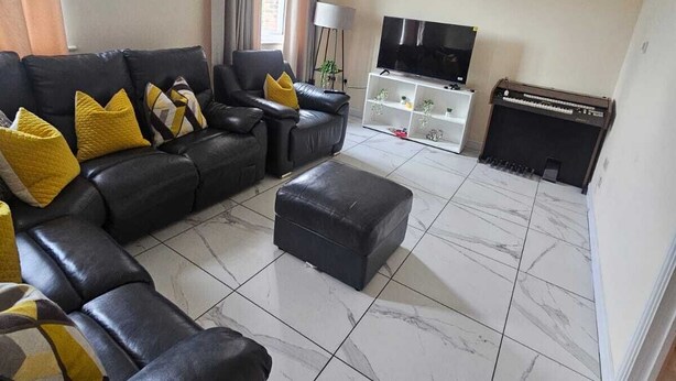 A living room with a sectional sofa, ottoman, flat-screen TV, piano, and a chandelier. - Sittingbourne Serenity - Spacious 4-bed House (Sittingbourne)