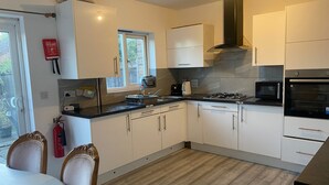 A modern kitchen with white cabinets, a black stove, and a microwave. There is a window with a view of greenery outside. - Sittingbourne Serenity - Spacious 4-bed House (Sittingbourne)