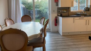 A dining area with a table and chairs, a kitchen with cabinets and a window, and a fire exit sign. - Sittingbourne Serenity - Spacious 4-bed House (Sittingbourne)