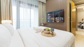 A hotel room with a large bed, a flat-screen TV mounted on the wall, and a breakfast tray with fruit and a glass. - Chic 2BR Urban Escape in Aykon City (Dubai)