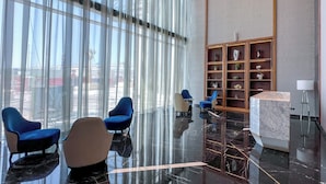A modern lobby with a marble floor, blue chairs, a marble reception desk, and a wooden display cabinet with decorative items. - Chic 2BR Urban Escape in Aykon City (Dubai)