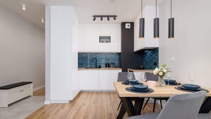 A modern kitchen with white cabinets, a blue backsplash, and a dining area with a wooden table and chairs.