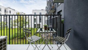 A balcony with two chairs and a table, overlooking a green garden and adjacent buildings.