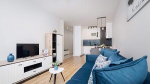 A modern living room with a blue sofa, a TV, and a small white table with a plant.