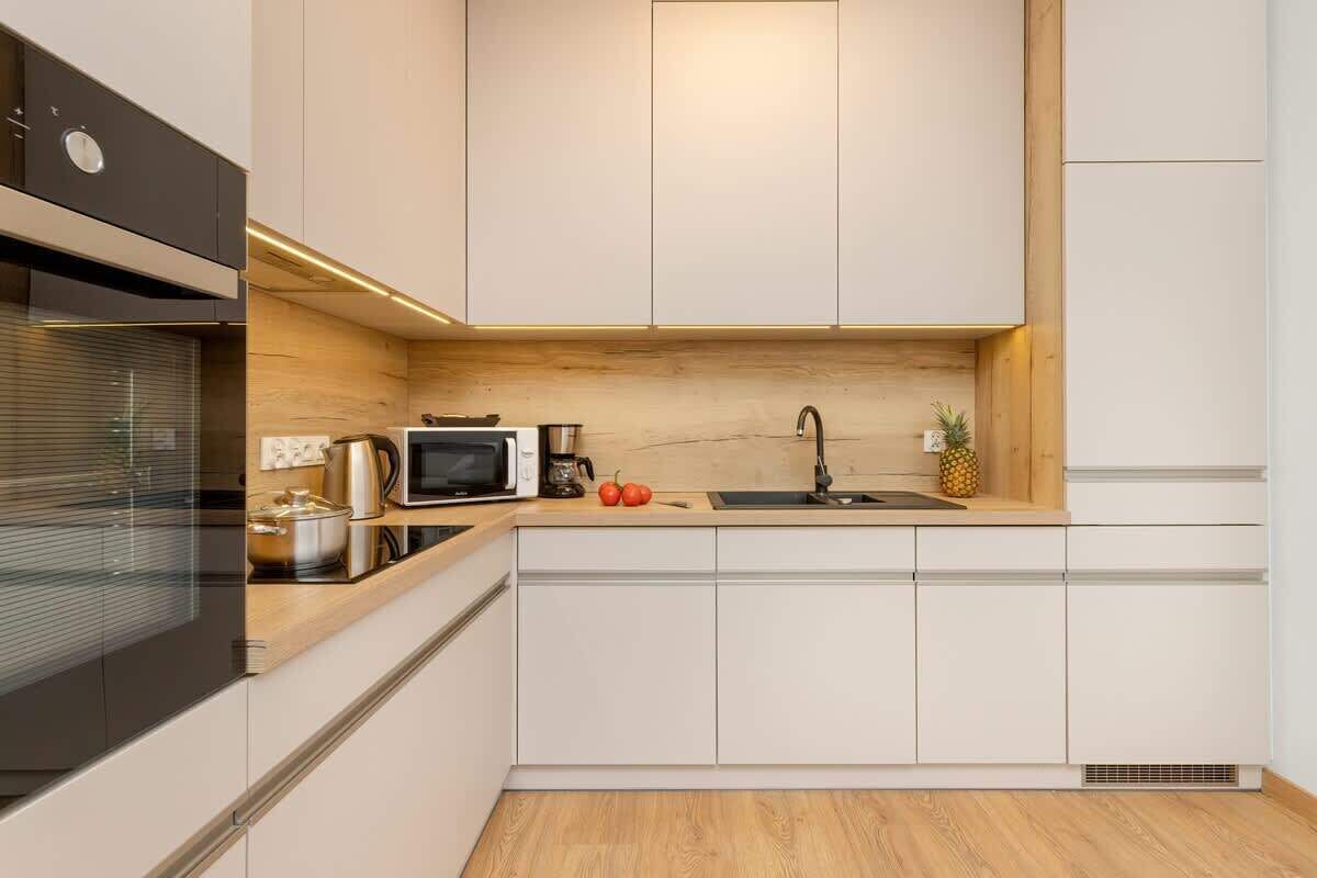 A modern kitchen with white cabinetry, a stainless steel range hood, a microwave, and a sink.
