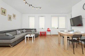 Un salon moderne avec un canapé gris, une petite table blanche, un fauteuil rouge et un coin repas comprenant une table en bois et des chaises noires.