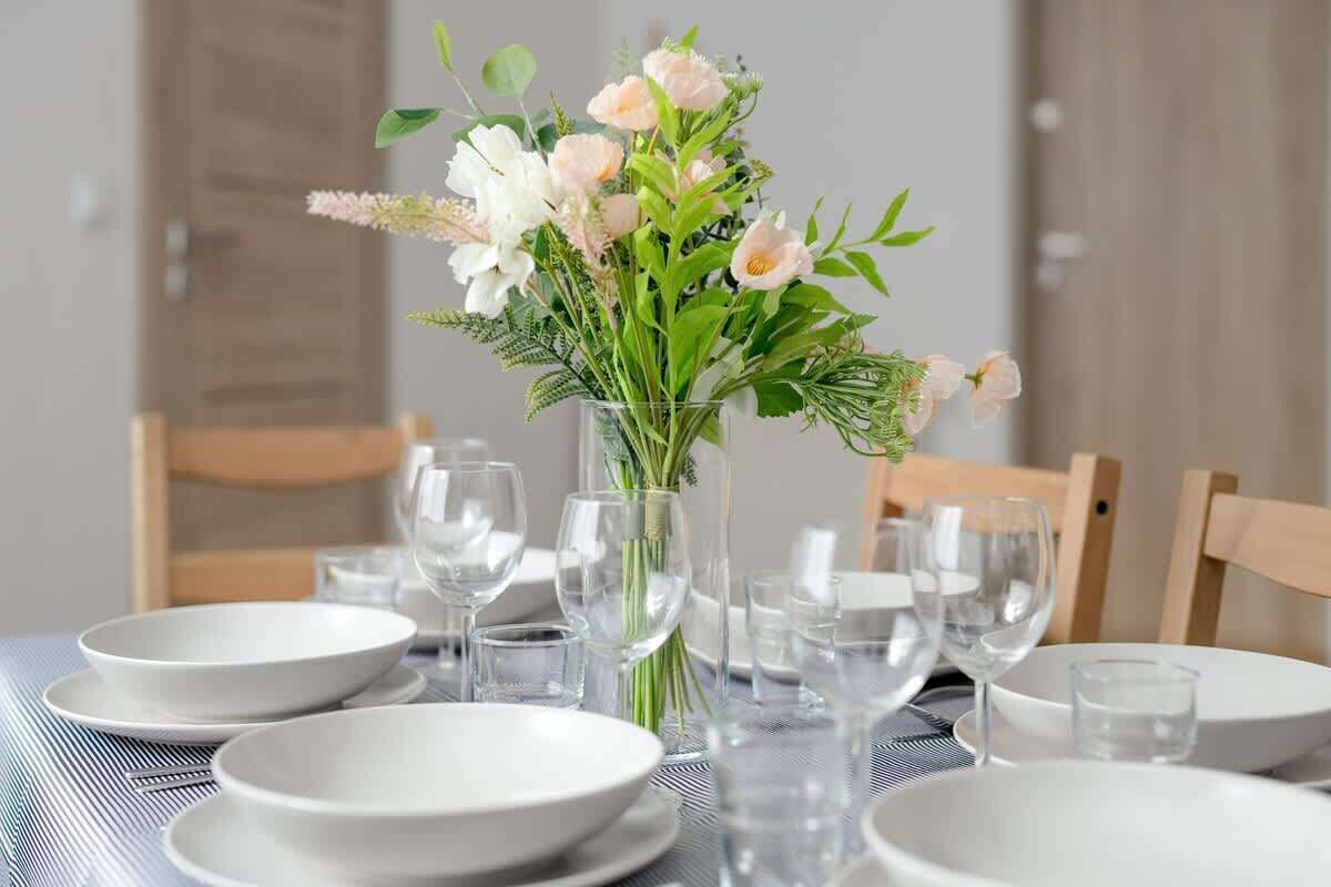 A dining table set with white plates, clear glasses, and a vase with flowers.