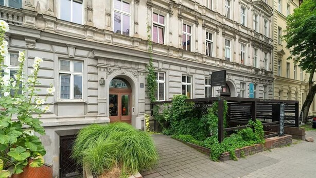 A historic building with a traditional facade, a gated entrance, and a small garden area with plants and a bench. - Elegancki i Stylowy Apartament Niedaleko Rynku w Poznaniu by Noclegi Renters (Poznan)