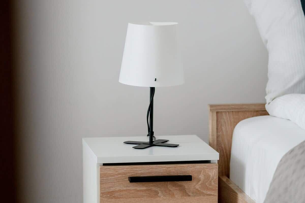 A modern bedside table with a white lamp and a drawer.