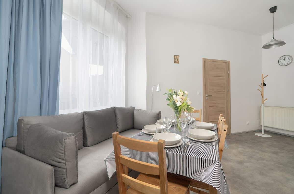 Ein Essbereich mit einem Tisch, gedeckt für vier Personen, einem grauen Sofa und einem Holzsessel.