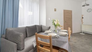 A dining area with a table set for four, a grey sofa, and a wooden chair. - Elegancki i Stylowy Apartament Niedaleko Rynku w Poznaniu by Noclegi Renters (Poznan)