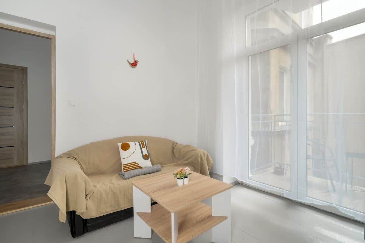 A modern living room with a beige sofa, a wooden coffee table, and a large window with a view of the outside.