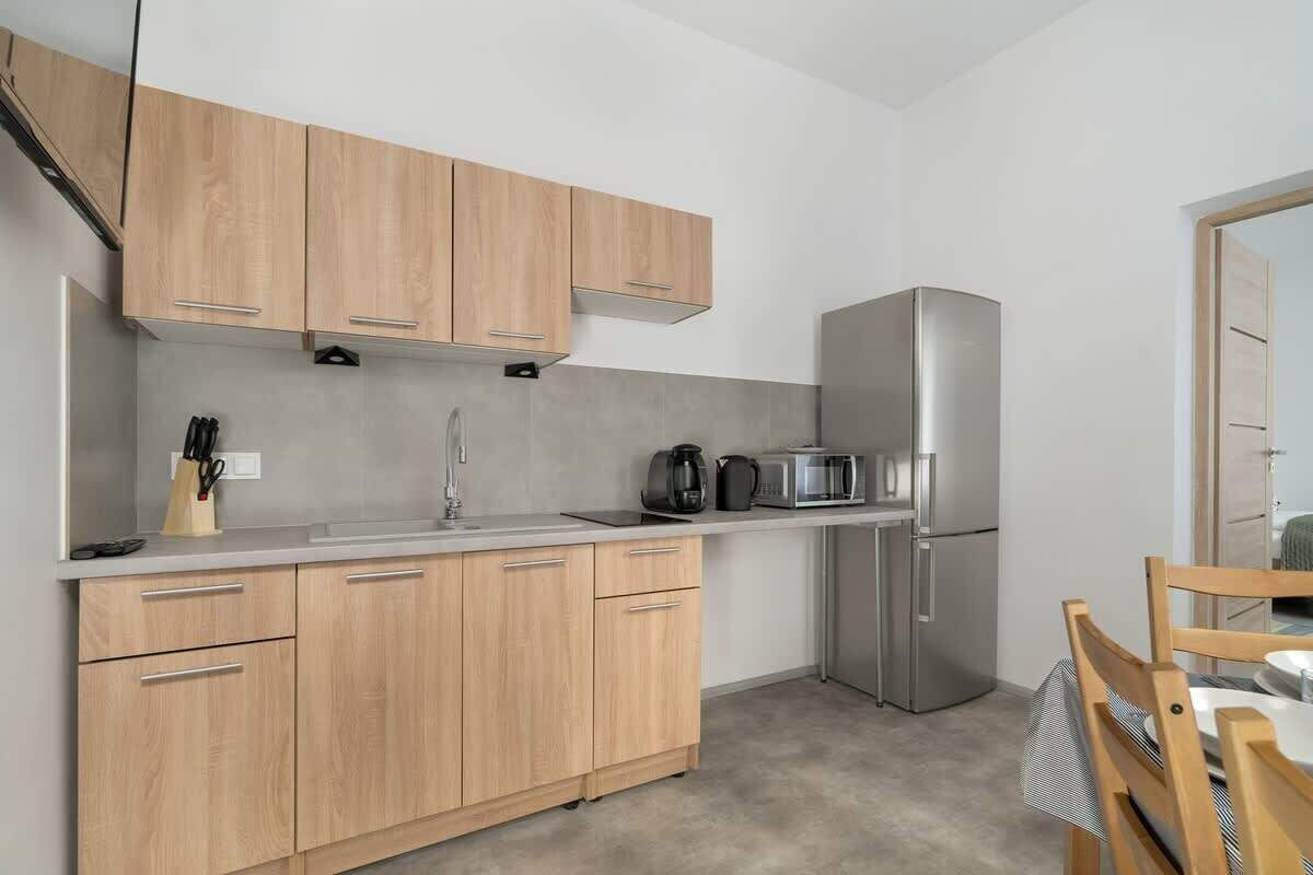 A modern kitchen with light wood cabinets, a stainless steel refrigerator, and a countertop with a coffee maker and toaster.