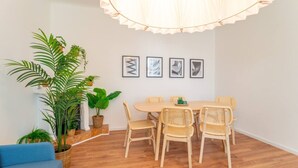 Un coin repas avec une table ronde et quatre chaises en osier, entouré de plantes en pot et de tableaux encadrés accrochés au mur.