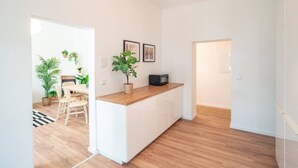 Une cuisine moderne avec des armoires blanches, un plan de travail en bois et un micro-ondes encastré. On peut voir des plantes en pot sur le plan de travail et un coin repas avec une table et des chaises à l’arrière-plan.