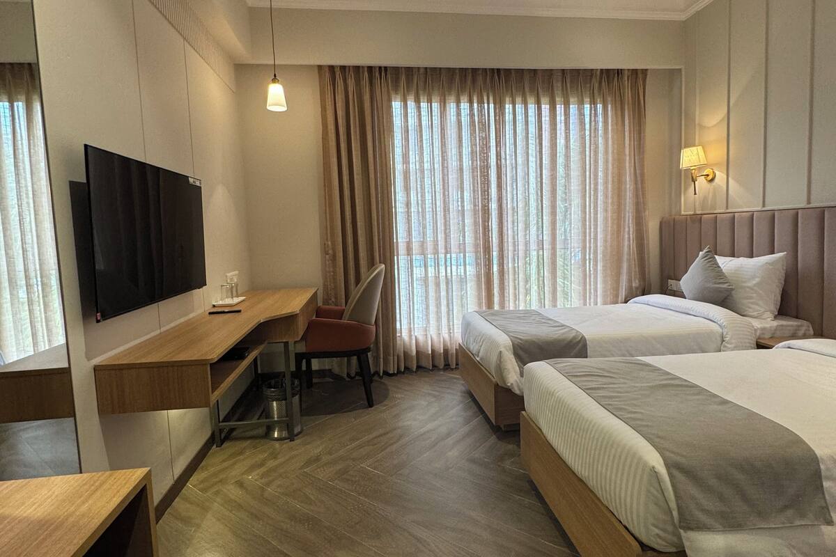 Ein Hotelzimmer mit zwei Betten, einem Schreibtisch, einem Sessel, einem Fernseher und einem Deckenventilator.