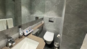 Un baño moderno con un espejo grande, un lavamanos, un inodoro y una zona de ducha.