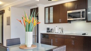 A modern kitchen with dark wooden cabinets, a stainless steel microwave, and a dining area with wicker chairs and a glass table.