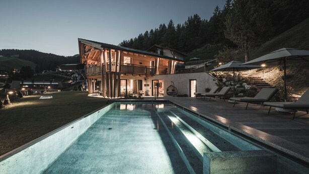 Una casa moderna de dos pisos con piscina, mobiliario exterior y vistas al bosque circundante.