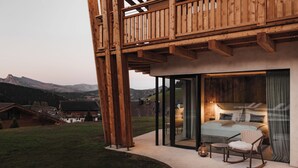 Una cabaña moderna de madera con un dormitorio con paredes de cristal, una mecedora y una pequeña mesa.