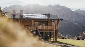 Una cabaña de madera con balcón, paneles solares y vistas a montañas.