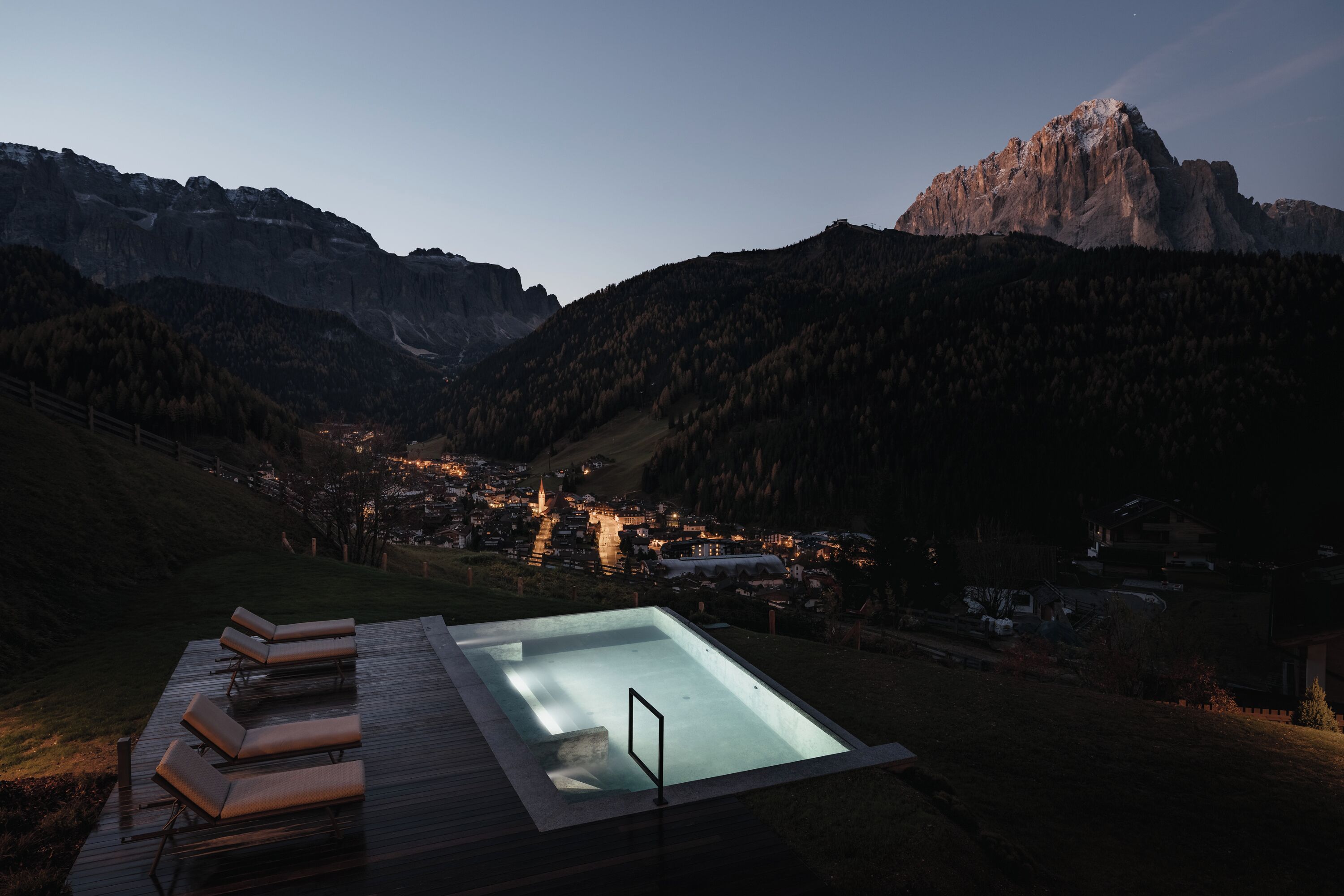 A pool area with lounge chairs, a view of a town, and mountains in the background.