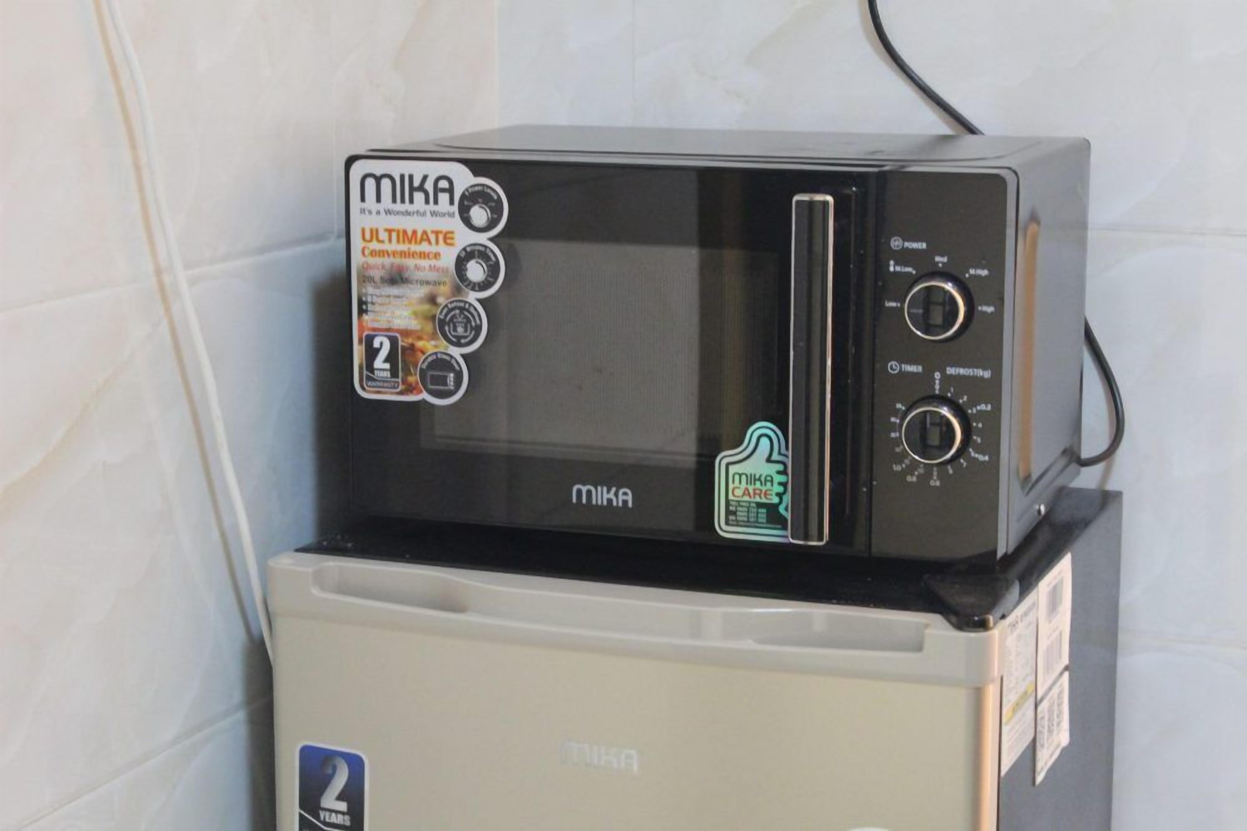 A compact microwave oven with a digital display and control panel, placed on top of a refrigerator.