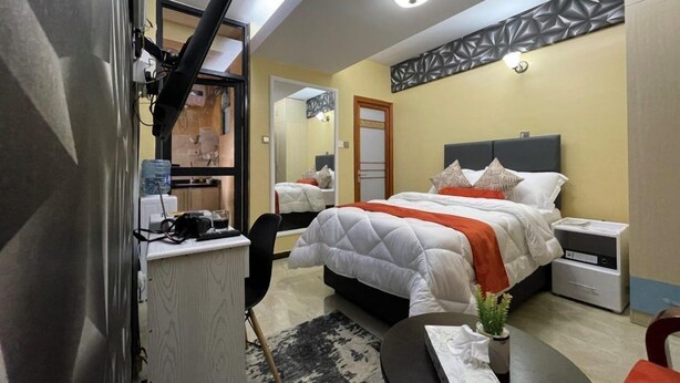 Une chambre d’hôtel avec un lit, des tables de chevet, un bureau avec une chaise, un miroir et une petite plante.