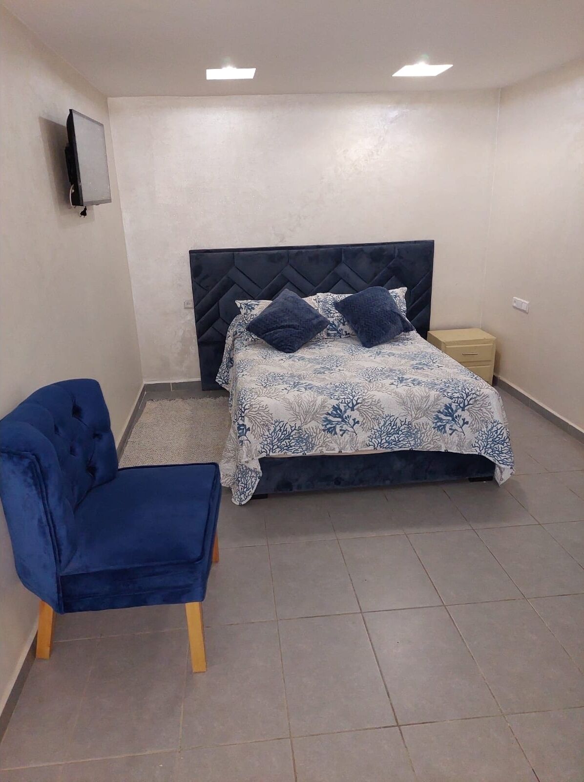 A bedroom with a bed, a blue chair, and a nightstand.