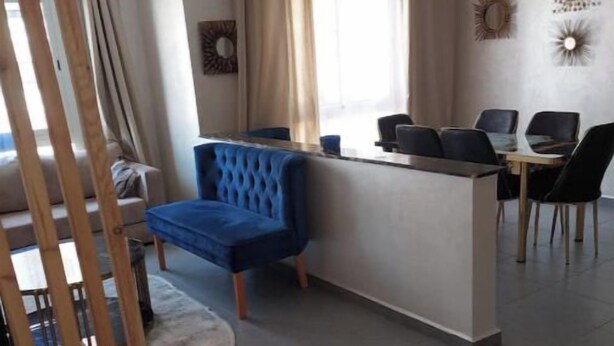 Un salon moderne avec un canapé bleu, un coin repas comprenant une table et des chaises, et un espace cuisine avec un comptoir.