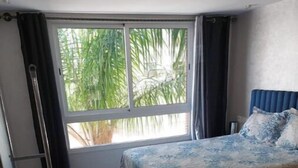 Une chambre à coucher avec un lit, une fenêtre avec des rideaux, une échelle et un sol carrelé.