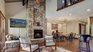 A spacious living area with a stone fireplace, comfortable seating, a dining table, and a large painting on the wall. - The Burly Bear | AC, Pool, Hot Tub, Golf & Ski (Durango)